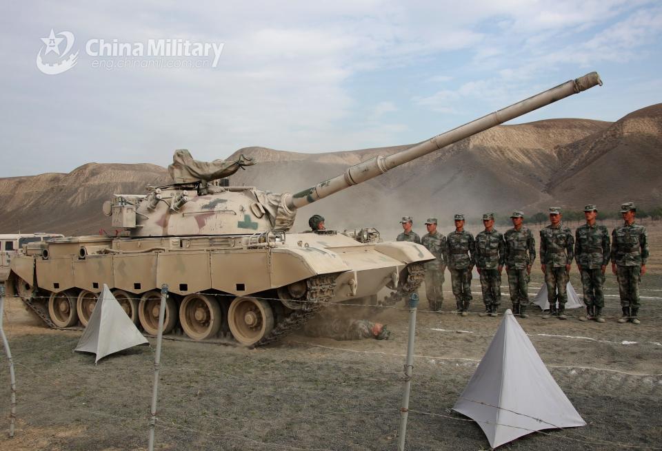 A soldier assigned to an army division under the PLA Xinjiang Military Command lies on the ground as a tank drives over him.