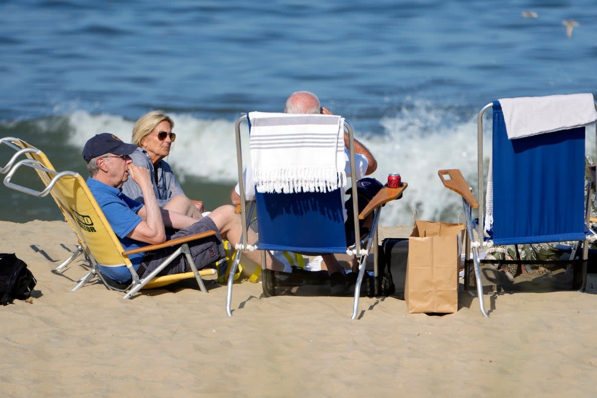 President Joe Biden, back to camera, sits with U.S. Ambassador to the European Union Mark Gitenstein, left, and first lady Jill Biden on the beach near his family home in Rehoboth Beach (AP)