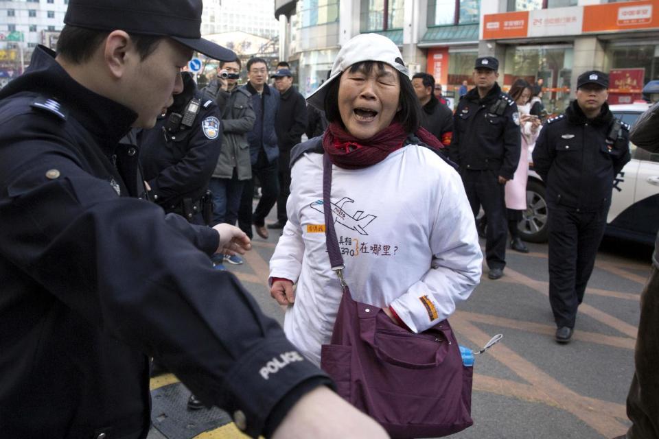 Dai Shuqin, whose younger sister and the sister's extended family were on board the missing Malaysia Airlines flight MH370 reacts as a policeman directs her to the pavement near the Foreign Ministry in Beijing, China, Wednesday, March 8, 2017. Wednesday marked the third anniversary of the disappearance of MH370, which vanished March 8, 2014 while en route from Kuala Lumpur to Beijing. (AP Photo/Ng Han Guan)