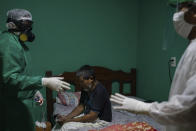 Plinio dos Santos, 65, who was having difficulty breathing, sits on his bed as emergency worker Wanden Nascimento, left, checks his oxygen saturation level before transferring him to a hospital in Manaus, Brazil, Wednesday, May 20, 2020. Dos Santos was admitted to the hospital, suspected of having COVID-19. (AP Photo/Felipe Dana)