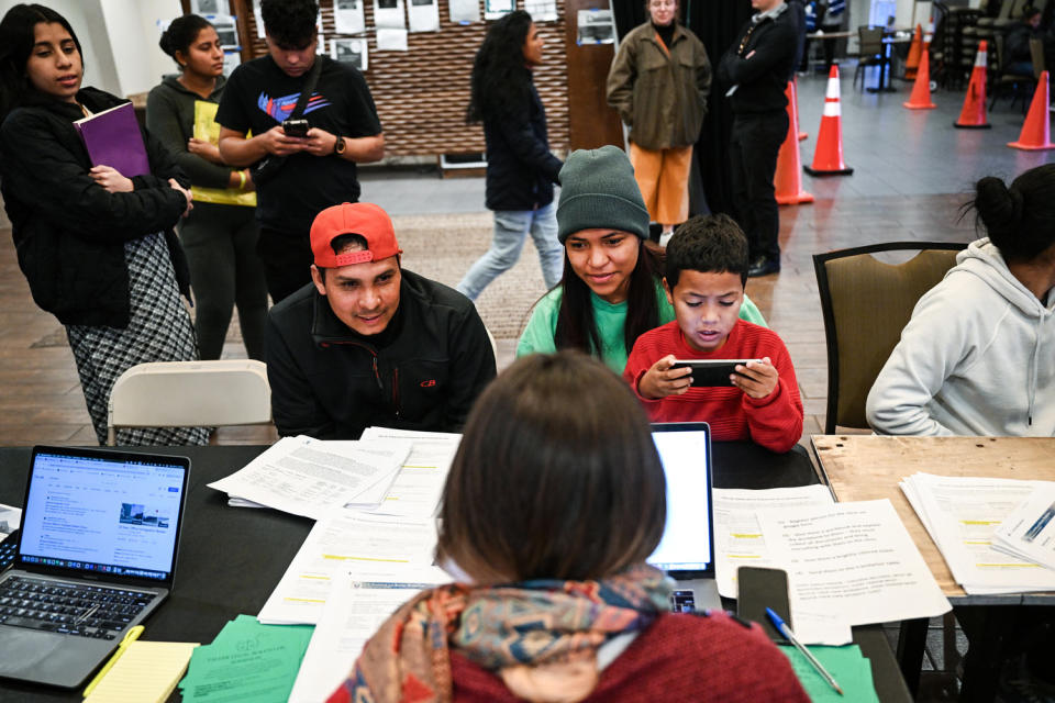 A volunteer, with back to camera, works with Venezuelan migrants at a computer desk layered with forms (Helen H. Richardson / The Denver Post via Getty Images file)