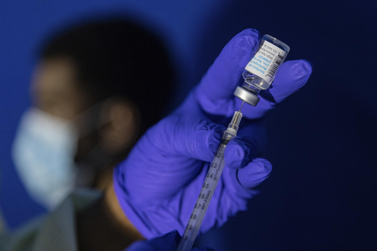 A gloved hand draws a vaccine into a syringe.