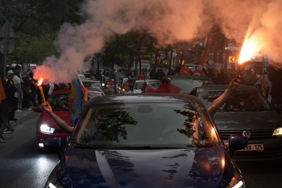 Two people hold blazing flares outside the windows of a car.