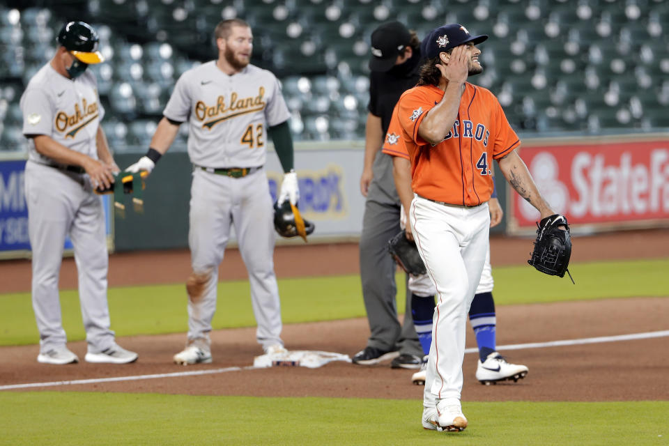 Oakland Athletics' Robbie Grossman stands on third base as Houston Astros starting pitcher Lance McCullers Jr., right, walks by after McCullers' throwing error to first base allowed a triple by him during the sixth inning of the first baseball game of a doubleheader Saturday, Aug. 29, 2020, in Houston. (AP Photo/Michael Wyke)