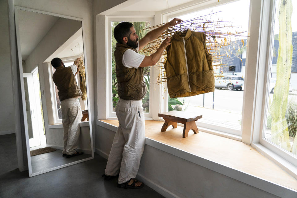 Clothing designer Max Kingery arranges a vest dyed naturally using wild mustard in his shop in the Venice neighborhood of Los Angeles, Thursday, June 15, 2023. Kingery is part of a growing group of artists, designers and chefs, who are tackling the invasion by harvesting the plant to use in everything from dyes to pesto. (AP Photo/Jae C. Hong)