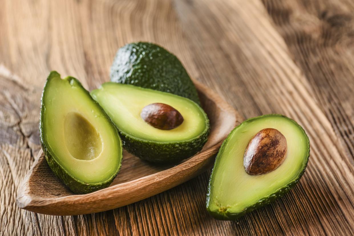 Avocado on old wooden table in bowl. Halfs of avocados fresh fruits healthy food.