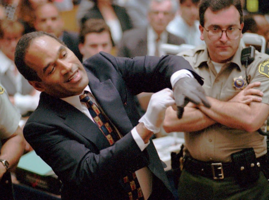 FILE – In this June 15, 1995 file photo, O.J. Simpson, left, grimaces as he tries on one of the leather gloves prosecutors say he wore the night his ex-wife Nicole Brown Simpson and Ron Goldman were murdered in a Los Angeles courtroom. Simpson, the decorated football superstar and Hollywood actor who was acquitted of charges he killed his former wife and her friend but later found liable in a separate civil trial, has died. He was 76. (Sam Mircovich/Pool Photo via AP, File)