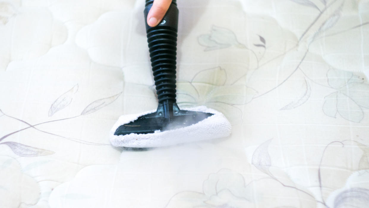  Person steam cleaning a white mattress to get rid of bed bug residue. 