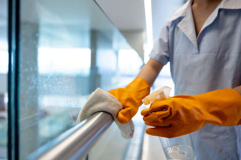 A person wearing orange gloves is cleaning a glass railing with a cloth and spray bottle