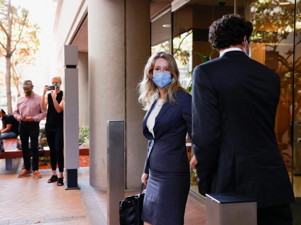 Theranos founder Elizabeth Holmes and her partner Billy Evans stand outside a courtroom with a crowd of people nearby