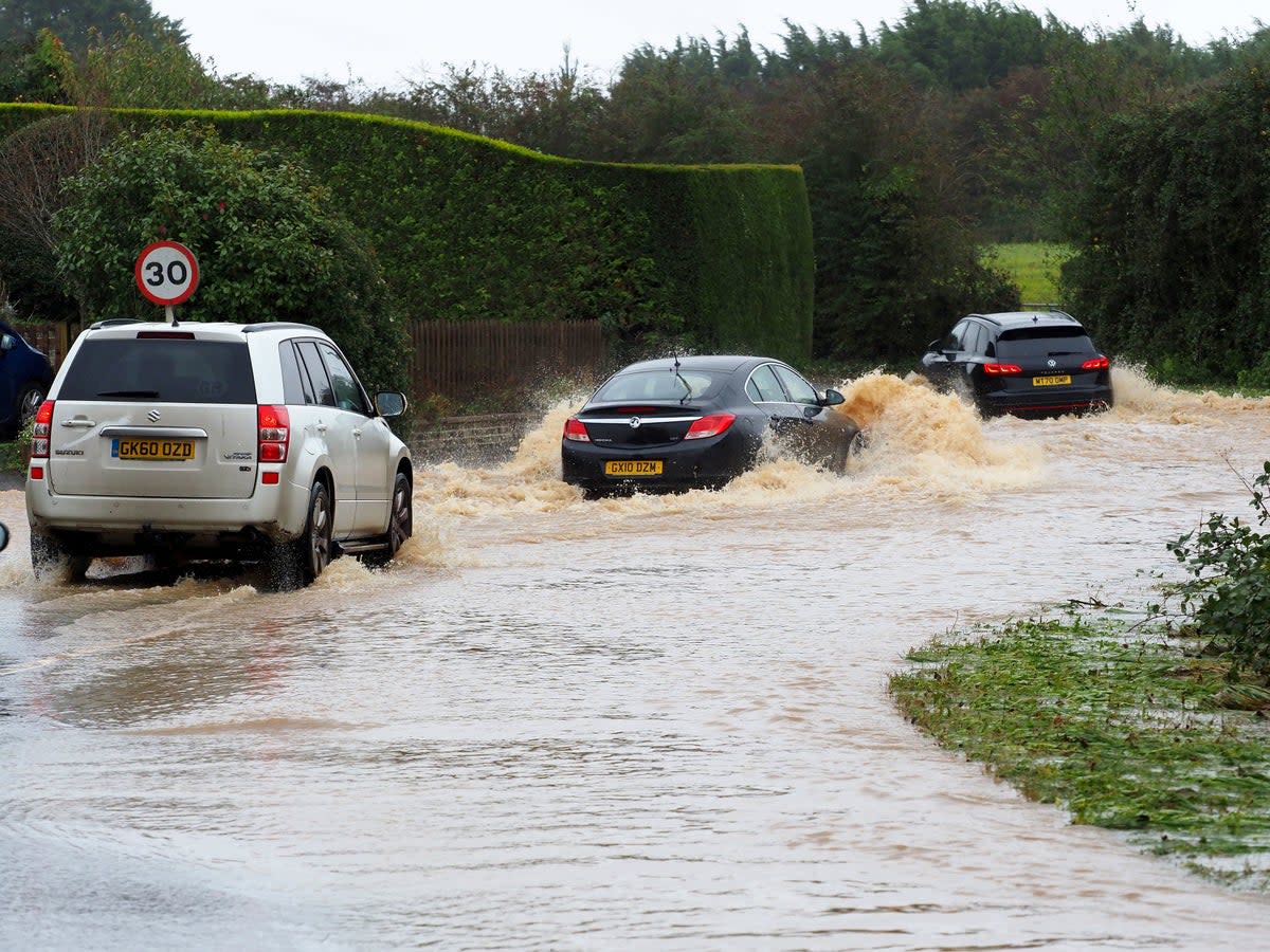 Vehicles drove through a flooded road in West Sussex (PA)