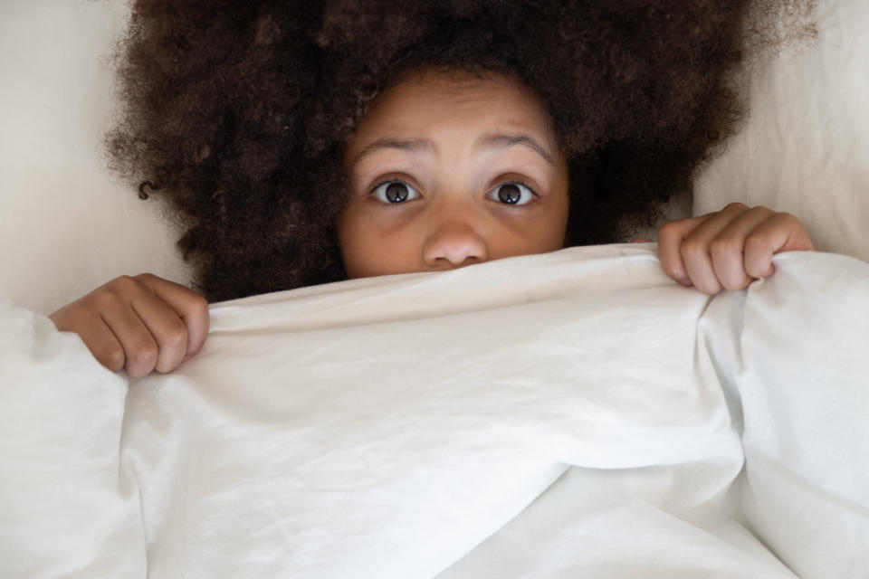 A child in bed pulls their covers close in fear
