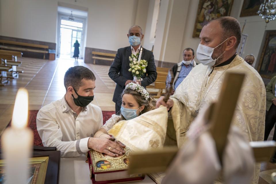 In this photo taken on Sunday, May 24, 2020, Father Vasyl Gasynets, Ukrainian Greek Catholic Church priest, right, conducts a religion service while Anatoliy Megeden and Svetlana Megeden swearing on the Holy Bible during their wedding ceremony at a church in Chernivtsi. Gasynets has returned to conducting services at his Greek Catholic church in priestly raiment, but wearing a mask while distributing communion. (AP Photo/Evgeniy Maloletka)