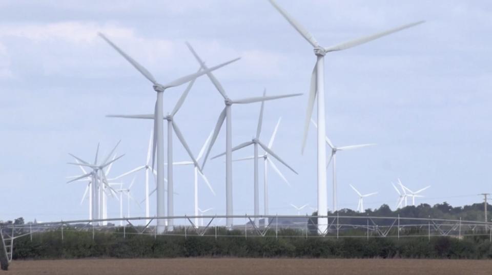 several wind turbines stand in a cluster in the countryside.