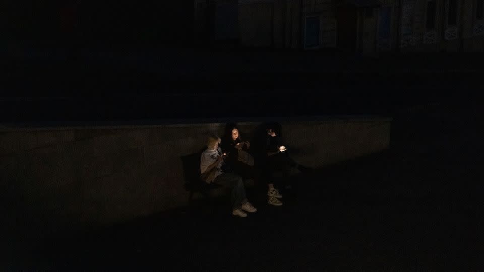 People sit on a bench as they check their smartphones in a street during a blackout following Russian attacks in Kharkiv, on April 8, 2024 - Roman Pilipey/AFP/Getty Images