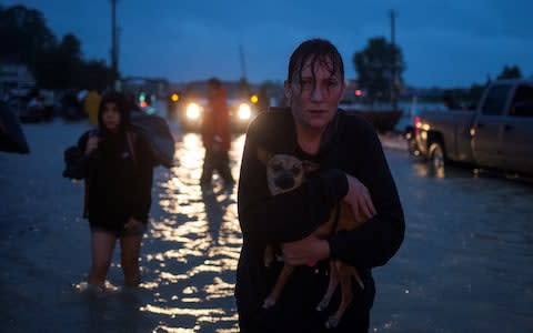 A woman holds her dog as she arrives to high ground - Credit: Reuters 