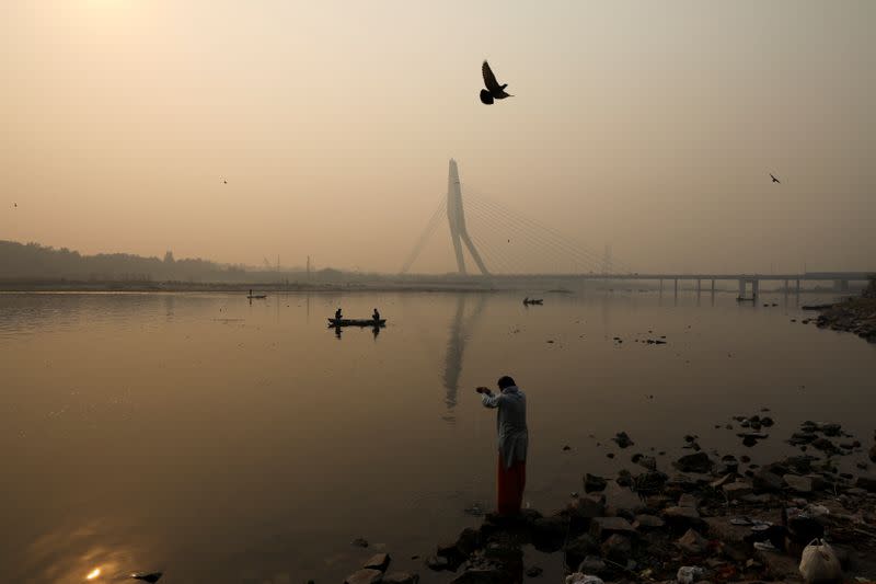 A man prays on the banks of Yamuna river, on a smoggy morning in New Delhi