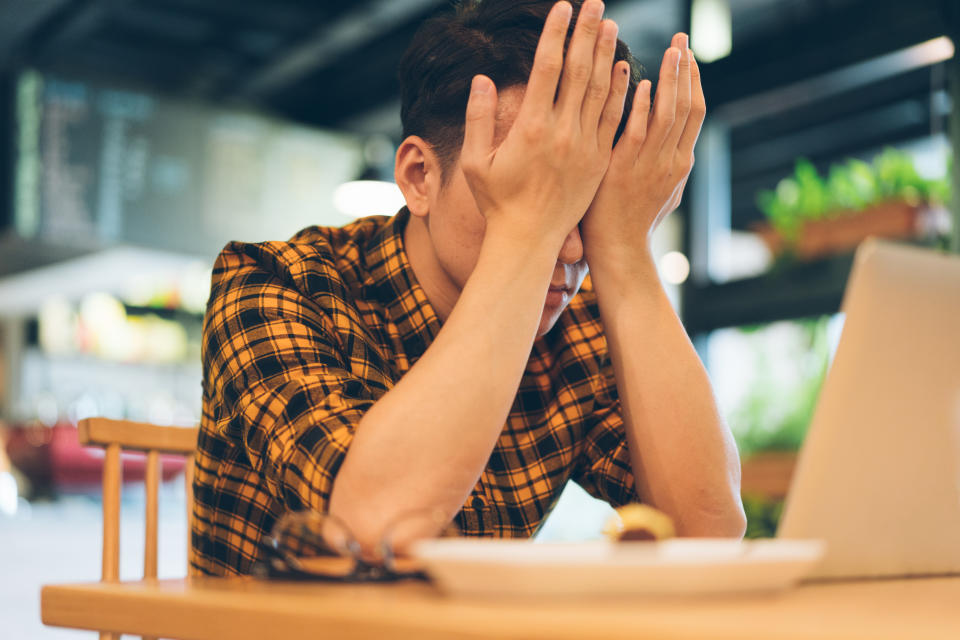 Exhausted young man rubbing eyes in cafe with laptop.