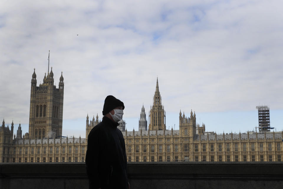 A man wears a face mask as he passes Britain's Parliament in London, Friday, Oct. 16, 2020. The British government is sticking to its strategy of tiered, regional restrictions to combat COVID-19 amid mounting political and scientific pressure for stronger nationwide measures to prevent the pandemic from spiraling out of control. (AP Photo/Kirsty Wigglesworth)