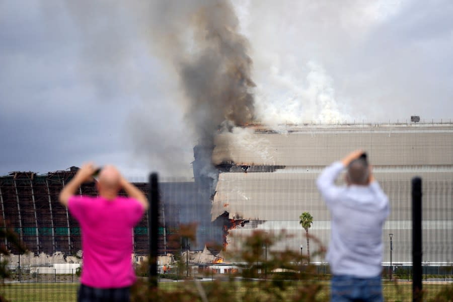 People take cell phone images as a historic blimp hangar burns in Tustin, Calif., Tuesday, Nov. 7, 2023. A fire destroyed a massive World War II-era wooden hangar that was built to house military blimps based in Southern California. (AP Photo/Jae C. Hong)