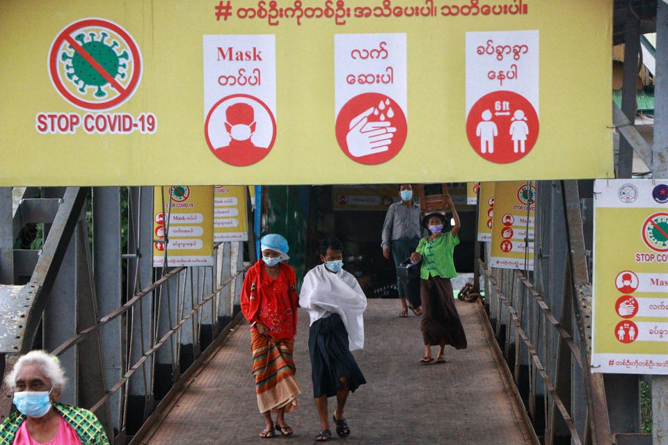 Ferry passengers wearing face masks walk past "Stop COVID-19" posters and banner at the Pansodan jetty in Yangon, Myanmar Tuesday, July 27, 2021. (AP Photo) ]