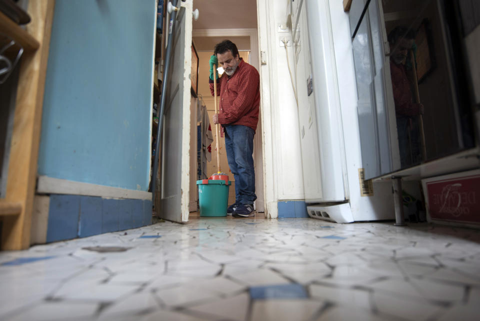 Joao Luiz Bulcao, 58, mops the kitchen floor on May 20, 2021, in the apartment in Montmartre, Paris, where he lives with his wife, Nathalie, and their two daughters. Bulcao, a Brazil-born photographer, traveled widely in Brazil, the United States and elsewhere during his career as a photographer but then found himself largely house-bound in Paris during the pandemic. Occasional payments of financial aid from the goverment helped the family make rent. With roots in both France and Brazil, Bulcao and his family feel fortunate to have weathered the pandemic in Paris. (AP Photo/Joao Luiz Bulcao).