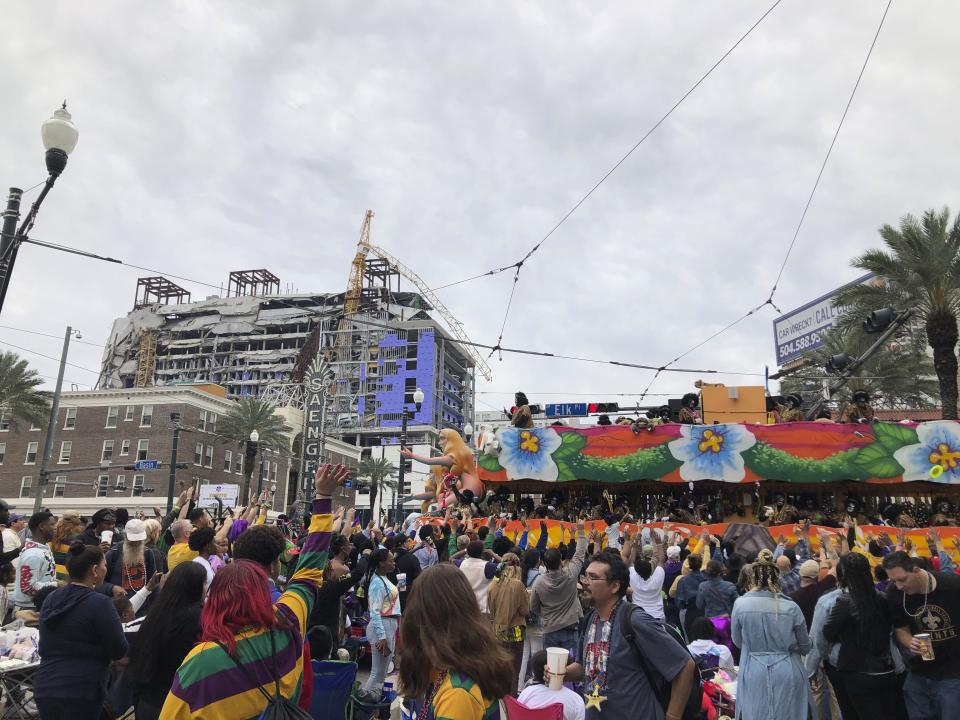 Crowds throng to catch beads and throws as the Zulu parade rolls through the streets of New Orleans on Tuesday, Feb. 25, 2020. In the background can be seen the remains of a hotel on the edge of the French Quarter that had been under construction when it partially collapsed in October. (AP Photo/Rebecca Santana)