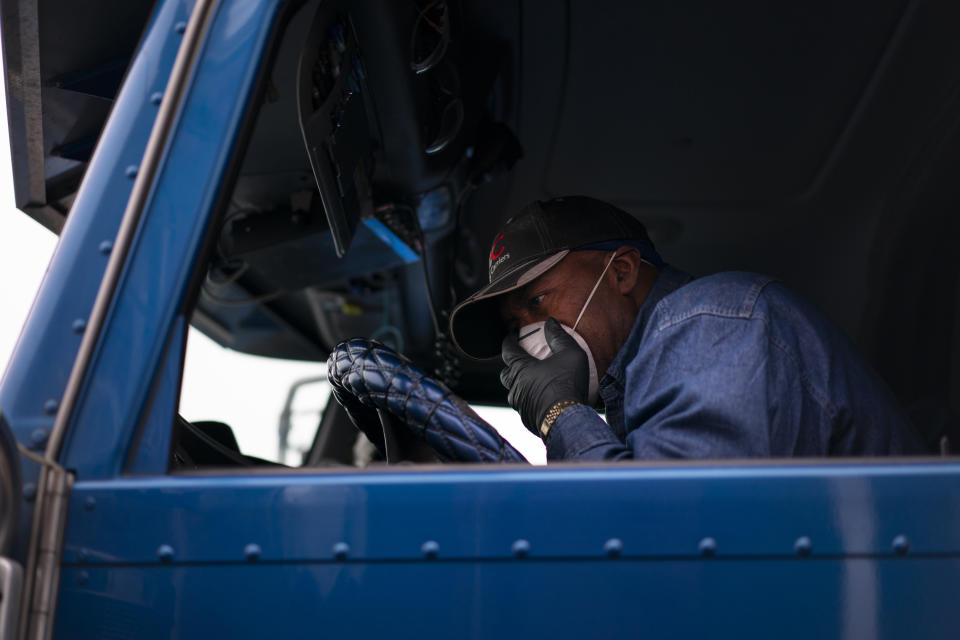 In this April 5, 2020, photo, with a gloved hand, trucker Allen Hall adjusts his face mask in the cab of his semitruck before rolling from the TA Travel Center truck stop in Foristell, Mo. Hall is doing his best to protect himself an others during the coronavirus outbreak. (AP Photo/Carolyn Kaster)