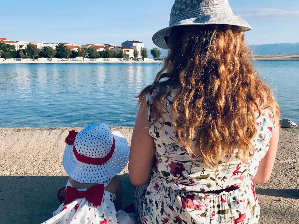 Woman and daughter wearing hats sitting by the water