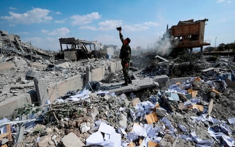 A Syrian soldier films the damage of the Syrian Scientific Research Center which was attacked by U.S, British and French military strikes - Credit: AP