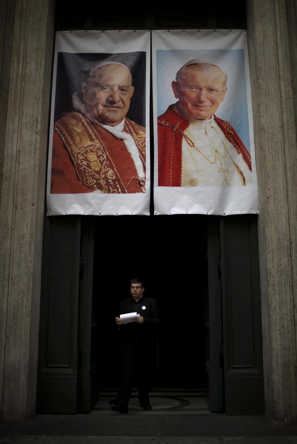 A priest stands in one of the entrances of the Saint Luigi dei Francesi (St. Louis of the French) church decorated with portraits of late Pope John Paul II and John XXIII during a mass in Rome, Saturday, April 26, 2014. Pilgrims and faithful are gathering in Rome to attend Sunday's ceremony at the Vatican where Pope Francis will elevate in a solemn ceremony John XXIII and John Paul II to sainthood. (AP Photo/Emilio Morenatti)