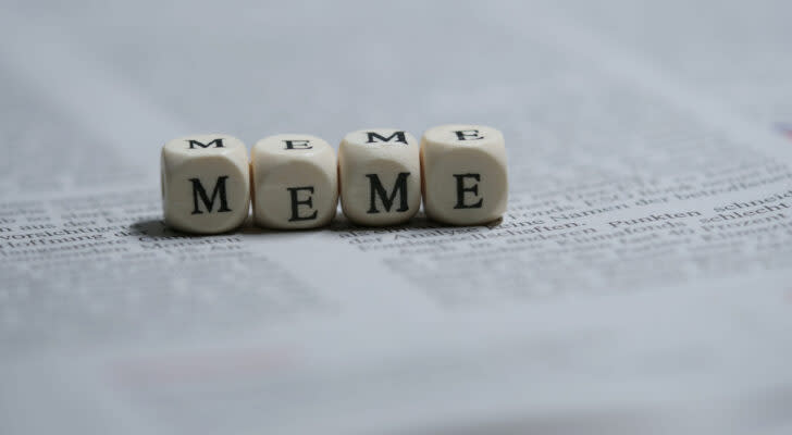 Four dice on a newspaper with letters instead of dots, spelling out the word "Meme". Meme Stocks to Sell