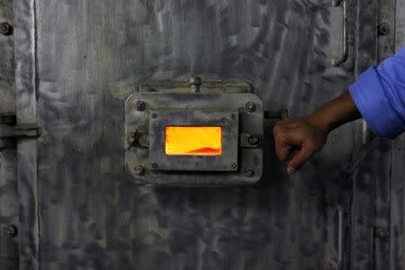 A worker holds open the window on the metal door of an incinerator at the Tuas South incineration plant in Singapore April 21, 2008. The plant incinerates waste into ash, which is then transported to Semakau Island and deposited into a landfill. The temperature in the incinerator exceeds 1000 degrees Centigrade (1832 degrees Fahrenheit). REUTERS/Vivek Prakash