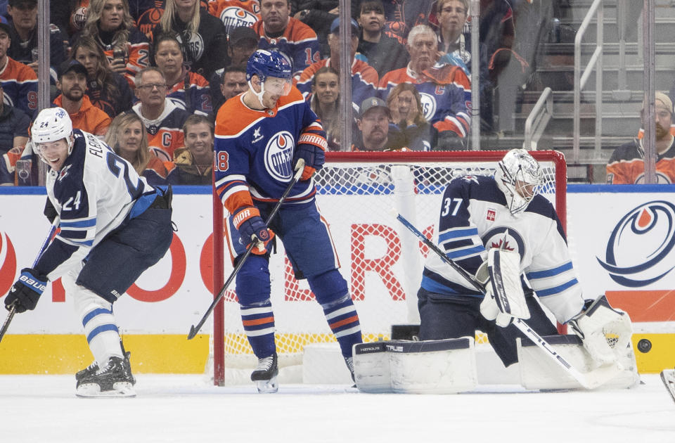 Winnipeg Jets goalie Connor Hellebuyck (37) makes a save as Edmonton Oilers' Zach Hyman (18) and Jets' Haydn Fleury (24) look on during the first period of an NHL hockey game, Wednesday, Oct. 9, 2024 in Edmonton, Alberta. (Amber Bracken/Canadian Press via AP)