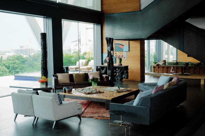 Two carved-wood totems by Nigerian Artist Reuben Ugbine preside over the living room. A pair of Ligne Roset armchairs, A børge Mogensen leather sofa, and a custom Poltrona Frau sofa surround a cocktail table by Jérôme Abel Seguin, who also crafted the mahogany root console at rear. Vintage Moroccan Rug from Nazmiyal Collection.