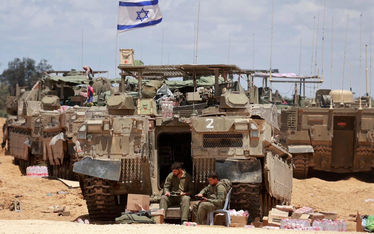 Israeli troops wait beside their tanks, flying an Israeli flag