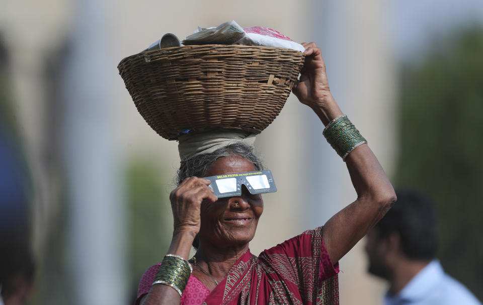 A roadside vendor holds a special filter and watches a partial solar eclipse in Hyderabad, India, Thursday, Dec. 26, 2019. (AP Photo/Mahesh Kumar A.)