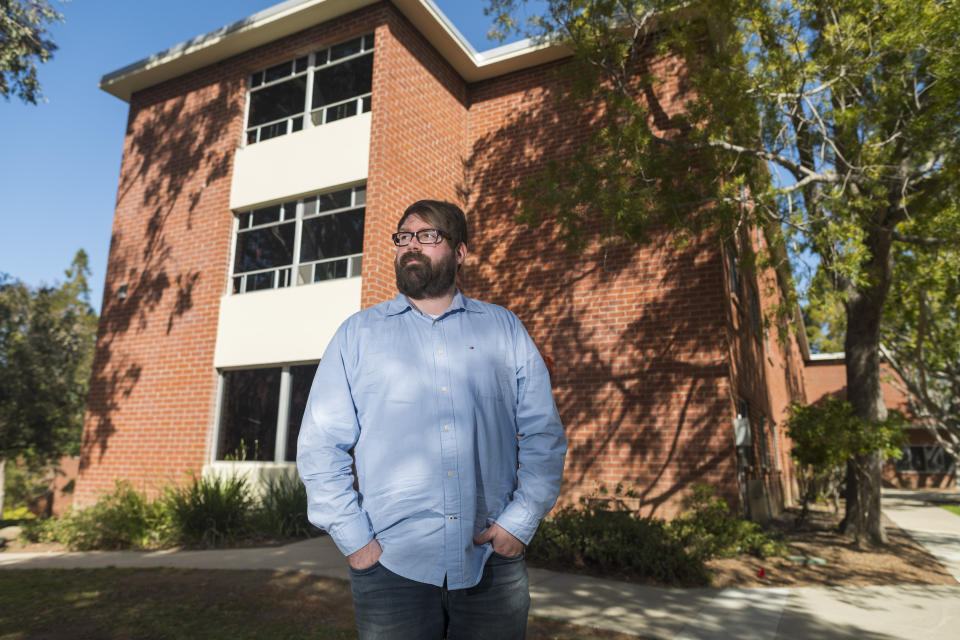 Chris Lambert, a musician and recording engineer, poses Thursday, April 15, 2021, in front of Muir Hall dormitory at California Polytechnic University in San Luis Obispo, Calif. Lambert started a podcast to document the 1996 disappearance of Kristin Smart, who was a college student at Cal Poly and lived in Muir Hall when she disappeared. On Tuesday, April 13, 2021, the San Luis Obispo County sheriff announced arrests in the 25-year-old case, crediting Lambert with helping bring in witnesses that propelled the case forward. (AP Photo/Nic Coury)