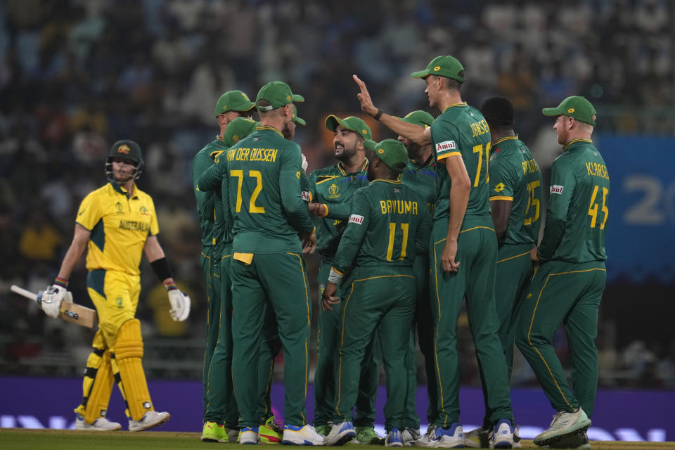 South African cricketers celebrate as Australia's Steve Smith, left, leaves the field after he was declared out by the third umpire during the ICC Cricket World Cup match between Australia and South Africa in Lucknow, India, Thursday, Oct. 12, 2023. (AP Photo/Altaf Qadri)