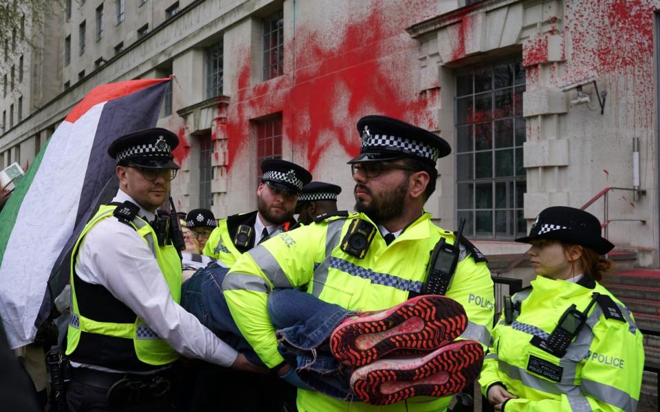 Police carry demonstrators away after the paint protest by groups Youth Demand and Palestine Action