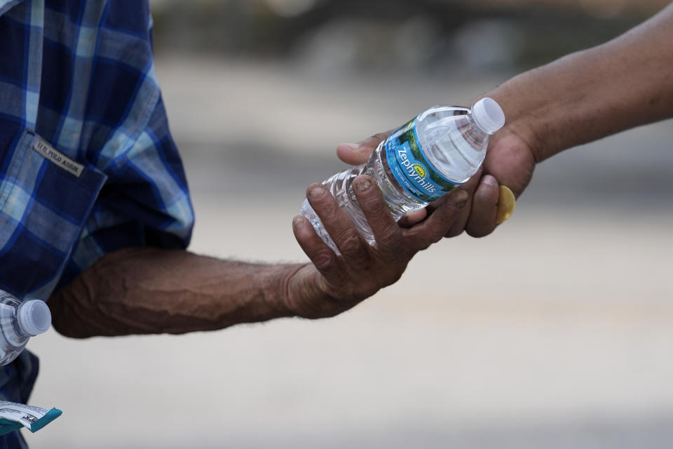 FILE - Ricky Leath, an outreach specialist with the City of Miami, right, hands a bottle of water to a person on the street as he works with the Miami-Dade County Homeless Trust to distribute water and other supplies to the homeless population, helping them manage high temperatures, May 15, 2024, in Miami. The Miami-Dade government and the local National Weather Service office team up to treat heat like hurricanes and emphasize advanced preparations. (AP Photo/Lynne Sladky, File)