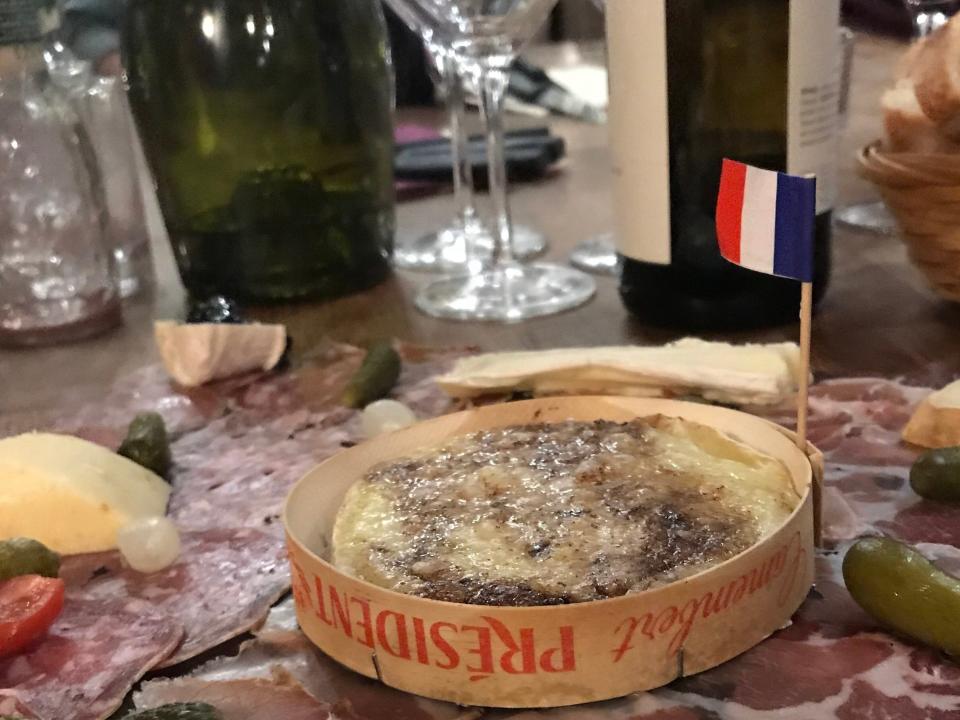 cheese board with pickes and bread and bottles of wine on the table behind it on a roof in paris