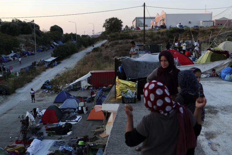 Migrants stand on a rooftop of a building as others remained camped out on a road leading from Moria to the capital of Mytilene, on the northeastern island of Lesbos, Greece, Thursday, Sept. 17, 2020. Fires swept through the overcrowded camp at Moria on two nights last week, prompting more than 12,000 migrants and refugees to flee. Most of them remain without shelter even though emergency tents are available at another island site where a new camp is being built. (AP Photo/Petros Giannakouris)