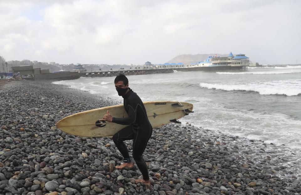 Wearing a face mask as a precaution amid the spread of the new coronavirus, Alejandro Torrealba gestures to the camera as he leaves the water on Waikiki Beach in the Miraflores district of Lima, Peru, Thursday, June 11, 2020. The emblematic surfers who dot Peru's coastline are retaking to the waves as the hard-hit nation relaxes COVID-19 related restrictions on outdoor sports. (AP Photo/Martin Mejia)