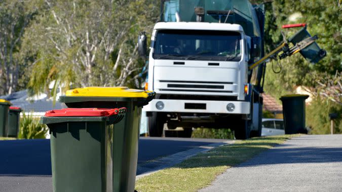 Focus on two Rubbish bins with rubbish truck in background lifting a bin.