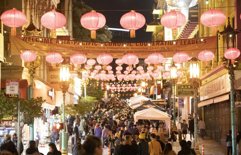 Many lanterns hang across a street crowded with people.