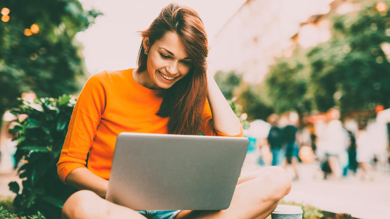 Beautiful happy woman texting and using a laptop outside in the city.