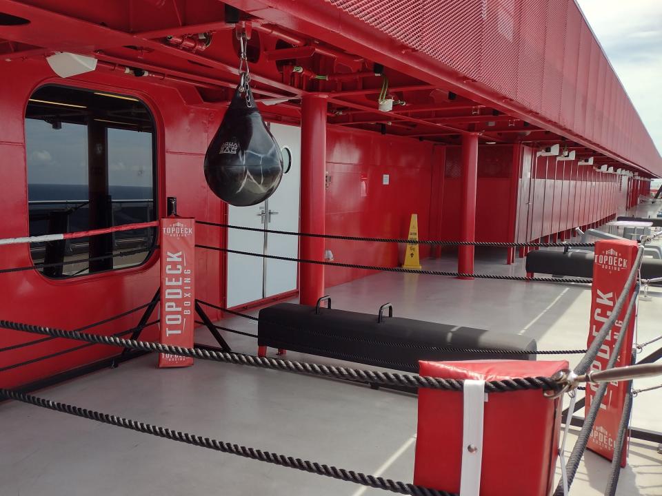 A boxing ring on a cruise ship surrounded by red walls, with a punching bag hanging.