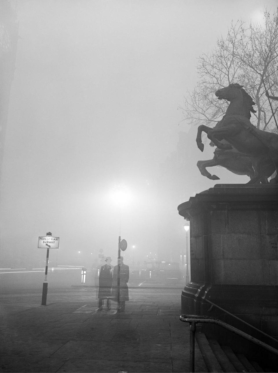 A statue of a horse and two pedestrians in the distance are obscured by smog in London on December 6, 1952.