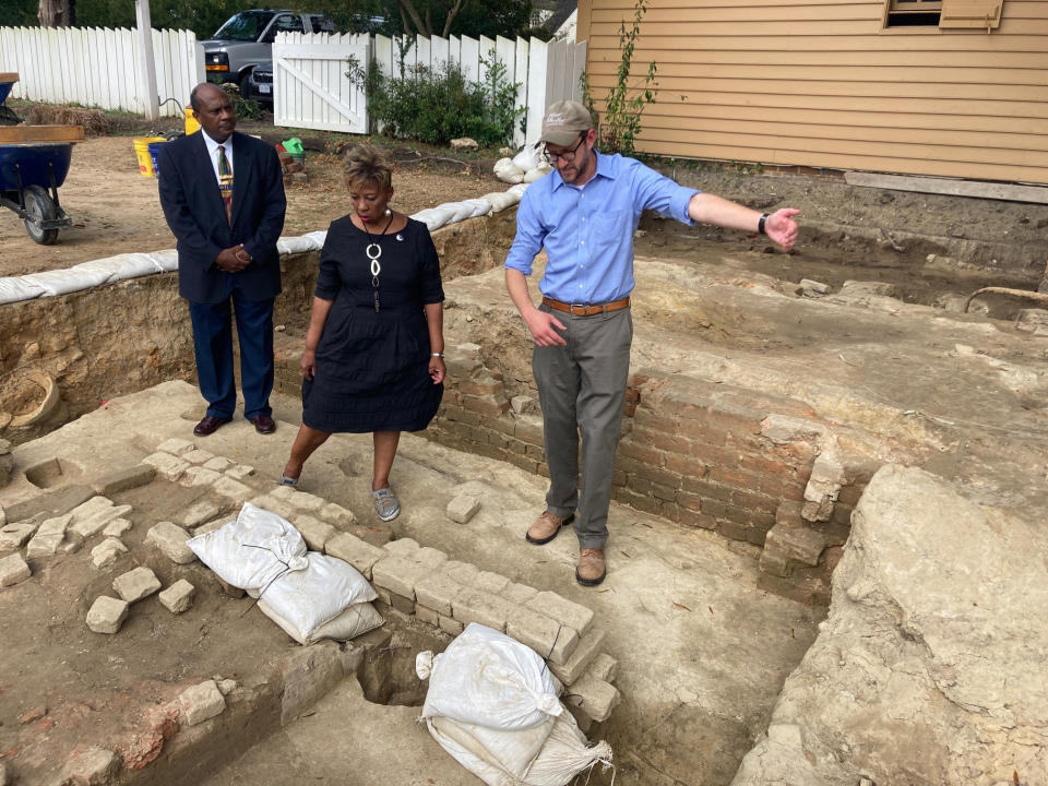 Reginald F. Davis, from left, pastor of First Baptist Church in Williamsburg, Connie Matthews Harshaw, a member of First Baptist, and Jack Gary, Colonial Williamsburg's director of archaeology, stand at the brick-and-mortar foundation of one the oldest Black churches in the U.S. on Wednesday, Oct. 6, 2021, in Williamsburg, Va. Colonial Williamsburg announced Thursday Oct. 7, that the foundation had been unearthed by archeologists. (AP Photo/Ben Finley)